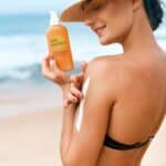 femeie la plaja cu flacon de protectie solara